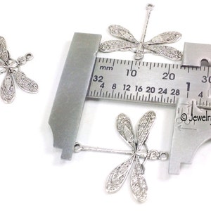 K&ouml;nnte beinhalten: Drei silberne Libellen-Anh&auml;nger mit einer &Ouml;se oben zum Anbringen an Schmuck. Die Anh&auml;nger werden mit einem Lineal gemessen und sind etwa 2 cm lang.