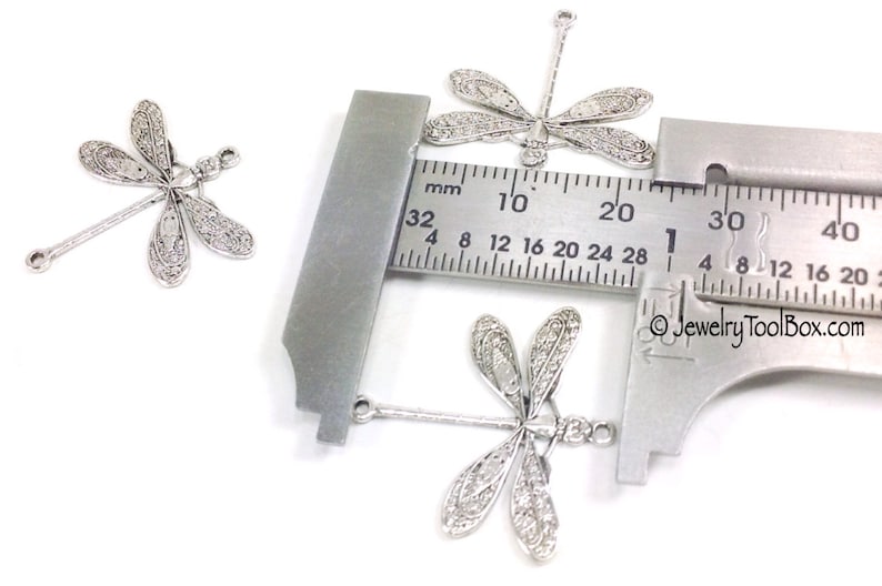 K&ouml;nnte beinhalten: Drei silberne Libellen-Anh&auml;nger mit einer &Ouml;se oben zum Anbringen an Schmuck. Die Anh&auml;nger werden mit einem Lineal gemessen und sind etwa 2 cm lang.