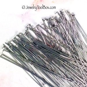 May include: A pile of silver-colored, straight, metal pins with a small loop at one end. The pins are approximately 1 inch long.