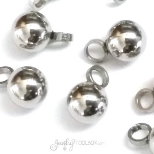 May include: Silver metal ball charms with a loop for attaching to jewelry. The charms are shiny and have a smooth surface.