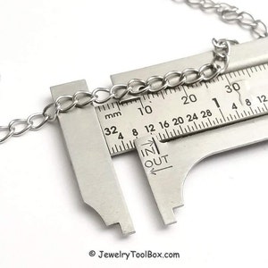 May include: A silver chain is measured with a ruler, showing a measurement of 20 mm. The ruler has markings in millimeters and inches.