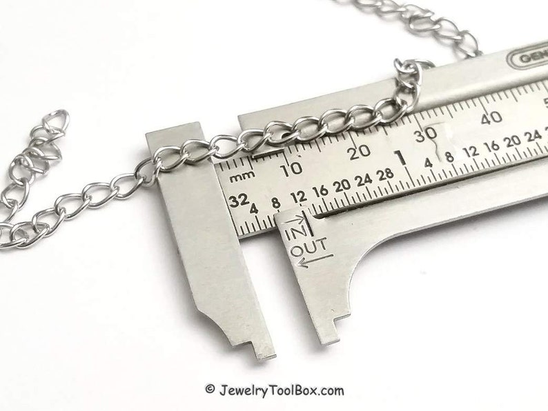 May include: A silver chain is measured with a ruler, showing a measurement of 20 mm. The ruler has markings in millimeters and inches.