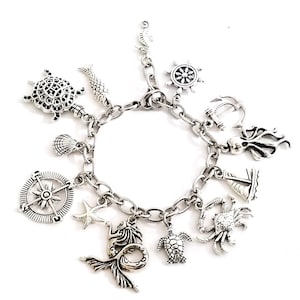 May include: A silver charm bracelet with a variety of nautical themed charms, including a compass, a mermaid, a turtle, a crab, a sailboat, an anchor, an octopus, a starfish, a seashell, and a fish.