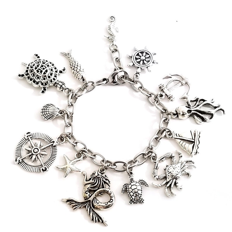 May include: A silver charm bracelet with a variety of nautical themed charms, including a compass, a mermaid, a turtle, a crab, a sailboat, an anchor, an octopus, a starfish, a seashell, and a fish.