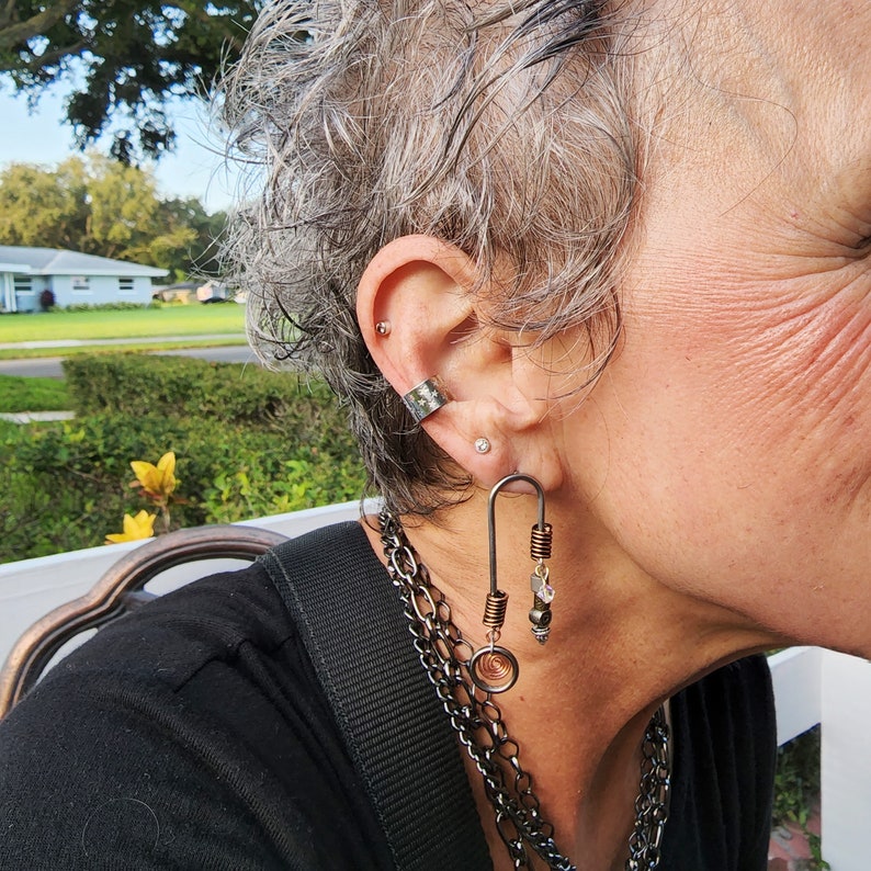 May include: A silver ear cuff and a long, dangling earring with a spiral design and copper and silver beads. The earring is worn in the left ear.