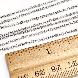 Puede incluir: Primer plano de eslabones de cadena plateados dispuestos sobre una regla de madera. La regla muestra medidas en pulgadas, con el n&uacute;mero "1" visible.