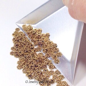Puede incluir: Primer plano de un mont&oacute;n de anillas de salto de metal de color dorado. Las anillas de salto son peque&ntilde;as y tienen un dise&ntilde;o delicado. Se est&aacute;n vertiendo desde una bandeja de metal.