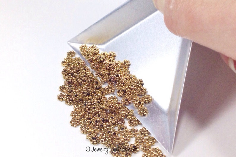Puede incluir: Primer plano de un mont&oacute;n de anillas de salto de metal de color dorado. Las anillas de salto son peque&ntilde;as y tienen un dise&ntilde;o delicado. Se est&aacute;n vertiendo desde una bandeja de metal.