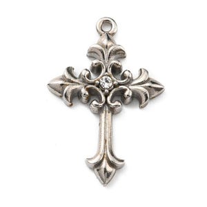 May include: Silver-toned metal cross pendant with ornate fleur-de-lis style arms and a small, clear crystal at the center. The pendant has a loop at the top for attaching to a chain or cord. The cross is a religious symbol.