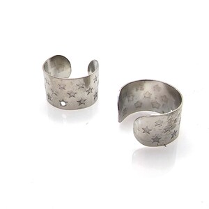 May include: A pair of silver ear cuffs with a star pattern. The cuffs are open and have a smooth, polished finish.
