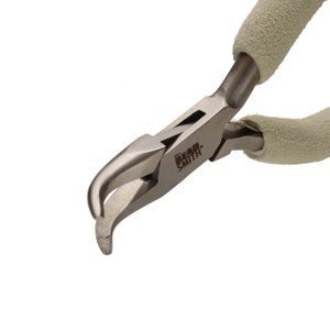 May include: Close-up of The Bead Smith brand pliers. The pliers are made of silver metal with a curved tip and light beige textured handles. The text "The Bead Smith" is printed on the side of the pliers.