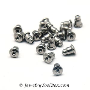 May include: A close-up of a pile of silver earring backs. The backs are small and round, with a hole in the center. They are designed to be used with post earrings.