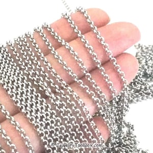 May include: A close-up of a silver chain, showing the chain's texture and detail. The chain is held in a hand, with multiple strands of the chain visible.