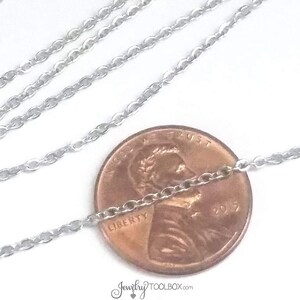 May include: A silver chain necklace laid out on a white surface with a US penny placed on top of the chain. The penny is dated 2017 and has the words "Liberty" and "In God We Trust" inscribed on it.