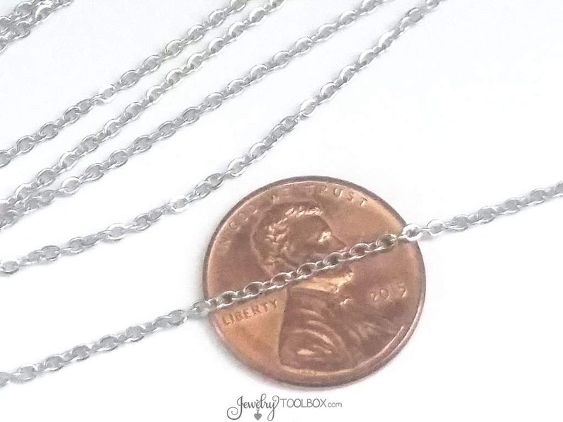 May include: A silver chain necklace laid out on a white surface with a US penny placed on top of the chain. The penny is dated 2017 and has the words "Liberty" and "In God We Trust" inscribed on it.