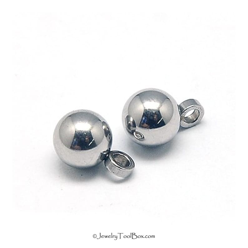 Puede incluir: Dos abalorios de metal plateado en forma de bola con un peque&ntilde;o bucle en la parte inferior. Las bolas son lisas y brillantes.