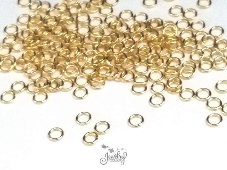 K&ouml;nnte beinhalten: Eine Ansammlung kleiner, kreisf&ouml;rmiger Metall-Biegeringe in Gold- und Silbert&ouml;nen. Die Ringe sind &uuml;ber das Bild verstreut und weisen ein einfaches, offenes Design auf. Das Logo von Jewelry Toolbox ist unten in der Mitte des Bildes zu sehen.