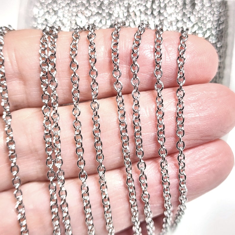 Puede incluir: Varias hebras de cadena plateada, mostradas en una mano, para la elaboraci&oacute;n de joyas.