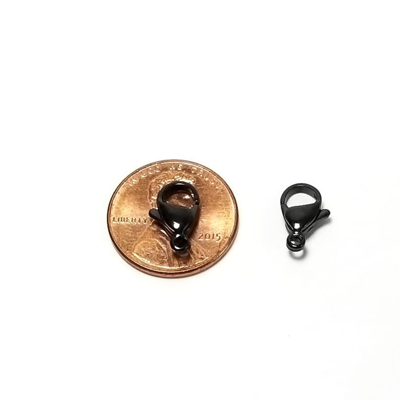 Puede incluir: Cierre de langosta de metal negro para la elaboraci&oacute;n de joyas, mostrado junto a un centavo estadounidense para comparar el tama&ntilde;o.