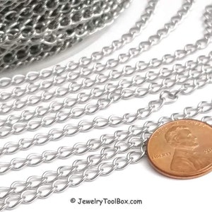 May include: Silver curb chain, a type of chain with a flat, rectangular link, is shown in a close-up image. The chain is laid out in rows, with a US penny placed on top of the chain for scale.