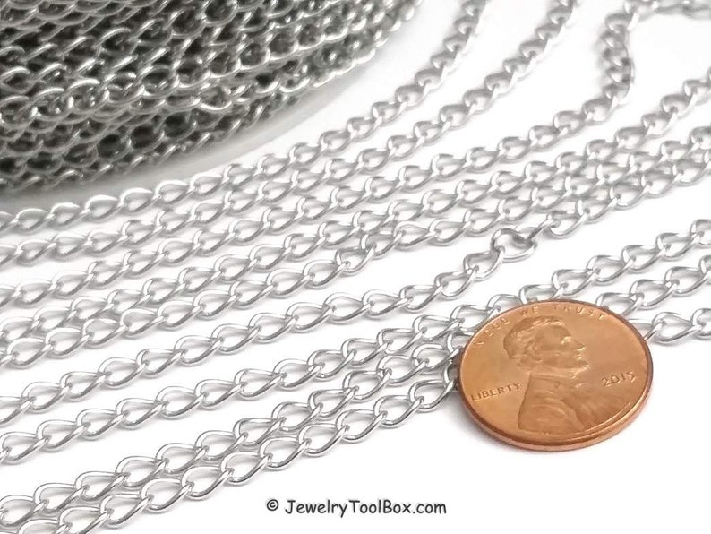 May include: Silver curb chain, a type of chain with a flat, rectangular link, is shown in a close-up image. The chain is laid out in rows, with a US penny placed on top of the chain for scale.