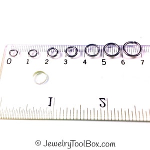 May include: A set of seven silver jump rings in various sizes, measured in inches on a ruler. The jump rings are arranged from smallest to largest, with the smallest ring measuring approximately 0.25 inches and the largest ring measuring approximately 0.75 inches.