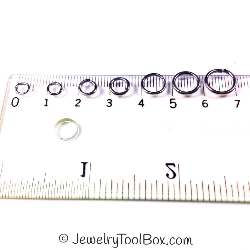 May include: A set of seven silver jump rings in various sizes, measured in inches on a ruler. The jump rings are arranged from smallest to largest, with the smallest ring measuring approximately 0.25 inches and the largest ring measuring approximately 0.75 inches.