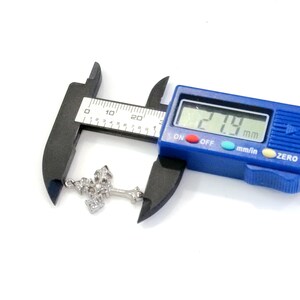 May include: A silver-colored cross pendant with a decorative design is measured with a blue digital caliper. The caliper displays a measurement of 21.9 mm. The cross is on a white background.
