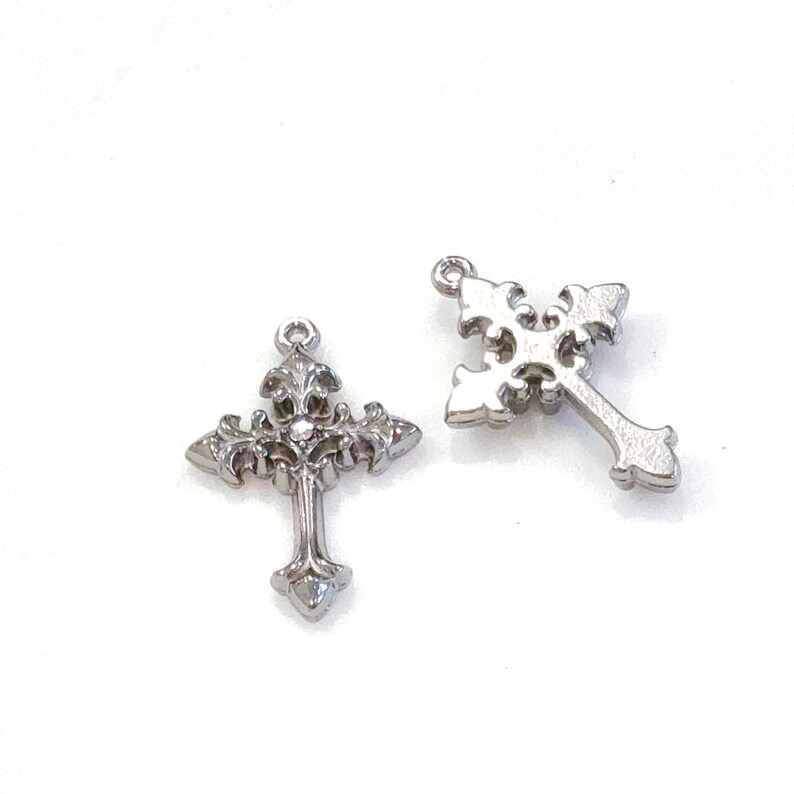 May include: Two silver-colored cross pendants with ornate designs. One cross features a detailed floral pattern at the top and center, while the other has a simpler, openwork design. Both have a loop at the top for hanging.
