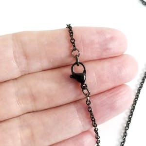 Puede incluir: Un collar de cadena negro con cierre de mosquet&oacute;n. La cadena es de metal y tiene un acabado mate.