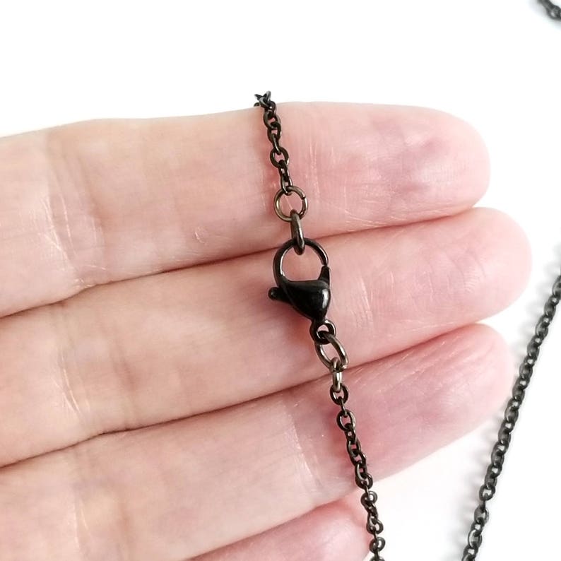 Puede incluir: Un collar de cadena negro con cierre de mosquet&oacute;n. La cadena es de metal y tiene un acabado mate.