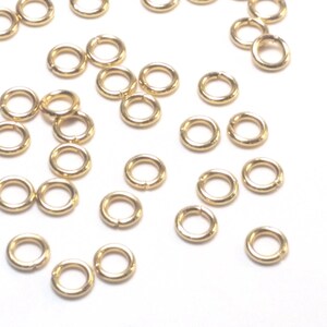 K&ouml;nnte beinhalten: Eine Ansammlung kleiner, kreisf&ouml;rmiger goldfarbener Metall-Biegeringe, die &uuml;ber den Rahmen verstreut sind. Jeder einzelne Ring besteht aus einem d&uuml;nnen, glatten Draht mit einer sichtbaren Nahtstelle, an der die beiden Enden aufeinandertreffen.