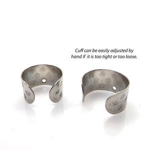 May include: Two silver ear cuffs with a star pattern. The cuffs are adjustable and can be easily tightened or loosened by hand.