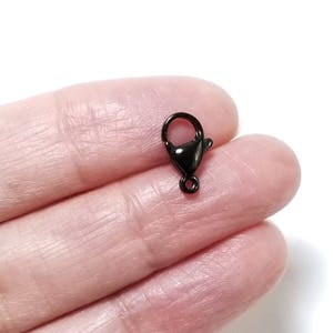 Puede incluir: Cierre de langosta de metal negro para la elaboraci&oacute;n de joyas. El cierre es peque&ntilde;o y tiene un acabado brillante.