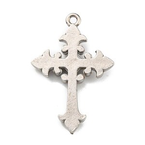 May include: A silver-colored cross pendant with an ornate, fleur-de-lis design. The cross features decorative curves and a loop at the top for hanging. The pendant is made of a metallic material and is set against a white background.