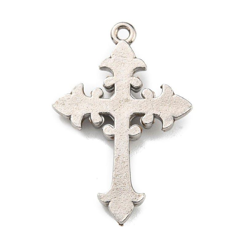 May include: A silver-colored cross pendant with an ornate, fleur-de-lis design. The cross features decorative curves and a loop at the top for hanging. The pendant is made of a metallic material and is set against a white background.