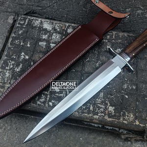 Può includere: Un coltello a lama fissa con lama in acciaio lucido, manico in legno scuro con perni in ottone e guardia argentata. Accanto si trova un fodero in pelle marrone scuro con cuciture bianche e chiusura a scatto. Il testo DELTAONE KNIVES & TOOLS è visibile.