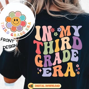 May include: Black t-shirt with a colorful retro design. The front features a flower with a smiling face and the text "Third Grade Era." The back displays "In My Third Grade Era" in vibrant, rounded letters. A digital download is available.