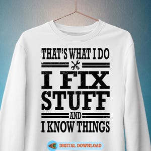 May include: White sweatshirt with the text "THAT'S WHAT I DO I FIX STUFF AND I KNOW THINGS" in black. A wrench and screwdriver graphic is between the first two lines of text. The sweatshirt is hanging on a gold hanger.