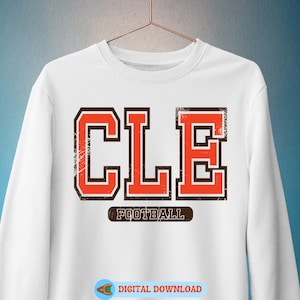 May include: White sweatshirt with the word "CLE" in orange and brown block letters. The word "FOOTBALL" is printed below the letters. The sweatshirt is hanging on a hanger.