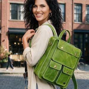 Könnte beinhalten: Ein leuchtend grüner Lederrucksack mit einer großen Klappentasche oben und zwei kleineren Taschen unten, die alle mit metallischen Druckknöpfen gesichert sind. Die Tasche verfügt über verstellbare Schultergurte und einen Tragegriff an der Oberseite.