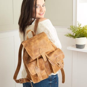 May include: A brown leather backpack with multiple pockets and adjustable straps. The bag has a flap closure and a drawstring. The leather has a distressed look. The backpack is being worn.