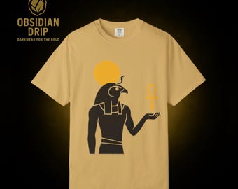 May include: Mustard yellow t-shirt featuring a black graphic of an Egyptian deity holding an ankh symbol. A yellow sun is behind the deity's head. The text "OBSIDIAN DRIP DARKWEAR FOR THE BOLD" is in the upper left corner.