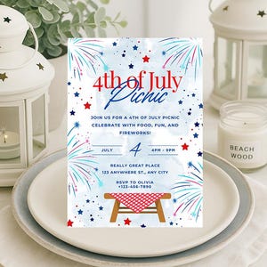 May include: A patriotic invitation for a 4th of July picnic, featuring a design with red, white, and blue fireworks and stars. The text reads "4th of July Picnic" and includes event details. The invitation is placed on a white plate with a white napkin, with a candle and lantern.