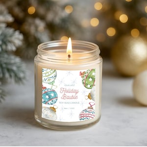May include: A lit soy wax candle in a clear glass jar. The label reads "Holiday Bauble" with watercolor illustrations of Christmas ornaments in blue, green, and red. The candle is 3 inches tall and 2.5 inches in diameter.