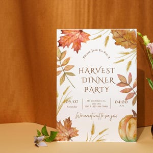 May include: A rectangular invitation for a Harvest Dinner Party, featuring watercolor illustrations of autumn leaves, wheat, and a pumpkin. The text includes the date, time, and RSVP information. A small brown vase holds a pink flower.