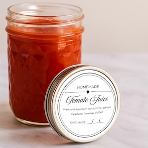 Könnte beinhalten: Ein Glas mit hausgemachtem Tomatensaft und einem Deckel daneben. Der Deckel trägt ein Etikett mit der Aufschrift "Homemade Tomato Juice" mit den Zutaten Tomaten und Salz. Das Glas steht auf einer hellen Oberfläche.