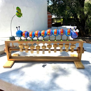 May include: A wooden abacus toy featuring a colorful caterpillar design. The caterpillar has blue, red, and yellow segments with green legs. A green and yellow butterfly is attached to the side. The abacus has wooden beads and a wooden frame.