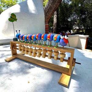 May include: A whimsical wooden caterpillar sculpture with colorful, round segments. Each segment is painted in vibrant hues of blue, red, and yellow, with large, googly eyes. The sculpture sits on a wooden frame with turning gears, creating a playful, kinetic art piece.