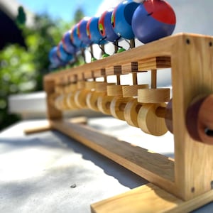 May include: A wooden abacus with a colorful caterpillar design. The caterpillar is made of painted wooden spheres in shades of blue, red, and purple. The abacus frame is made of light-colored wood, with wooden beads for counting.